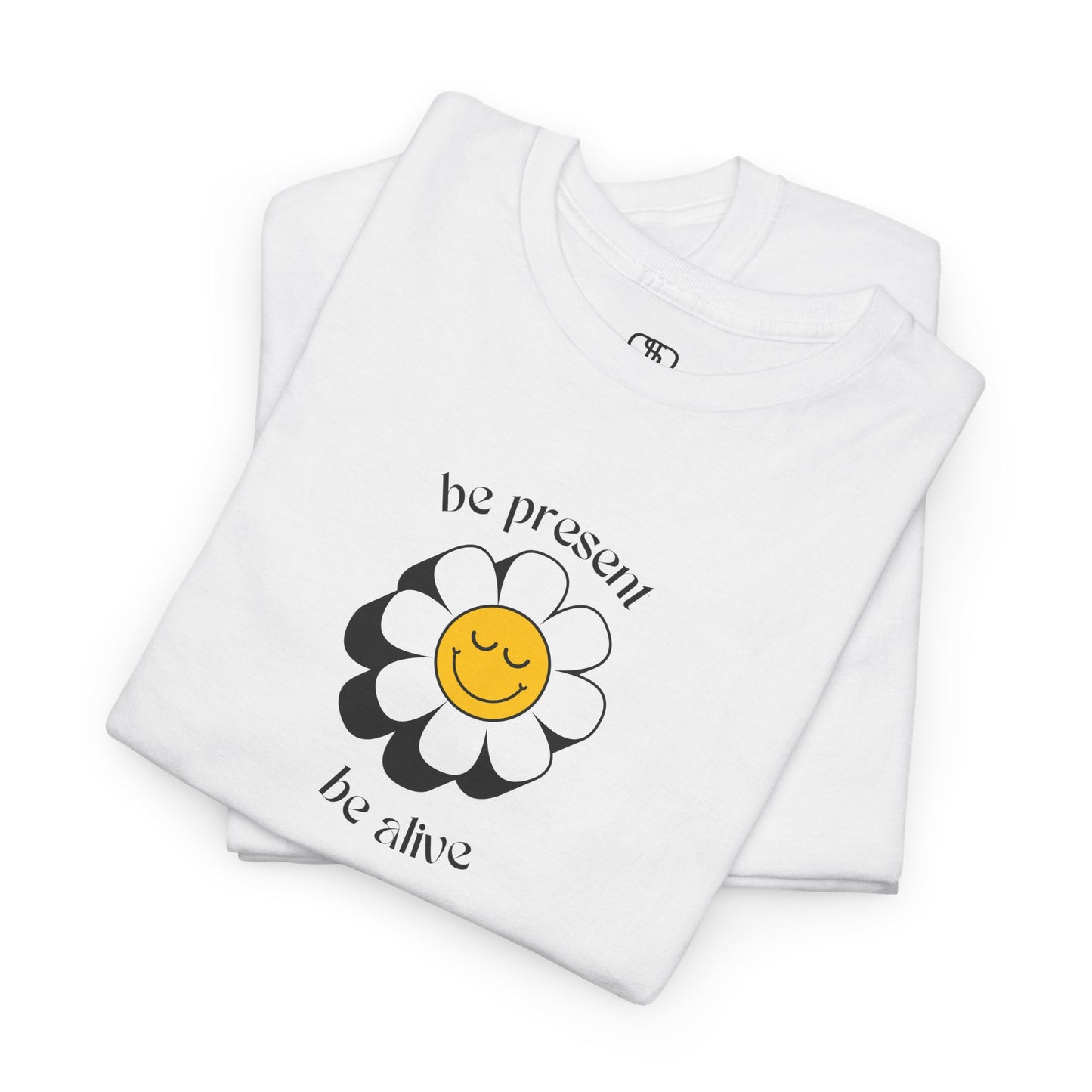 A vibrant yellow sunflower graphic on a folded white t-shirt. The inspirational phrase “Be Present, Be Alive” is elegantly integrated into the design.
