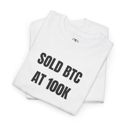 A Folded white T-shirt with bold text "SOLD BTC At 100K" on the front.