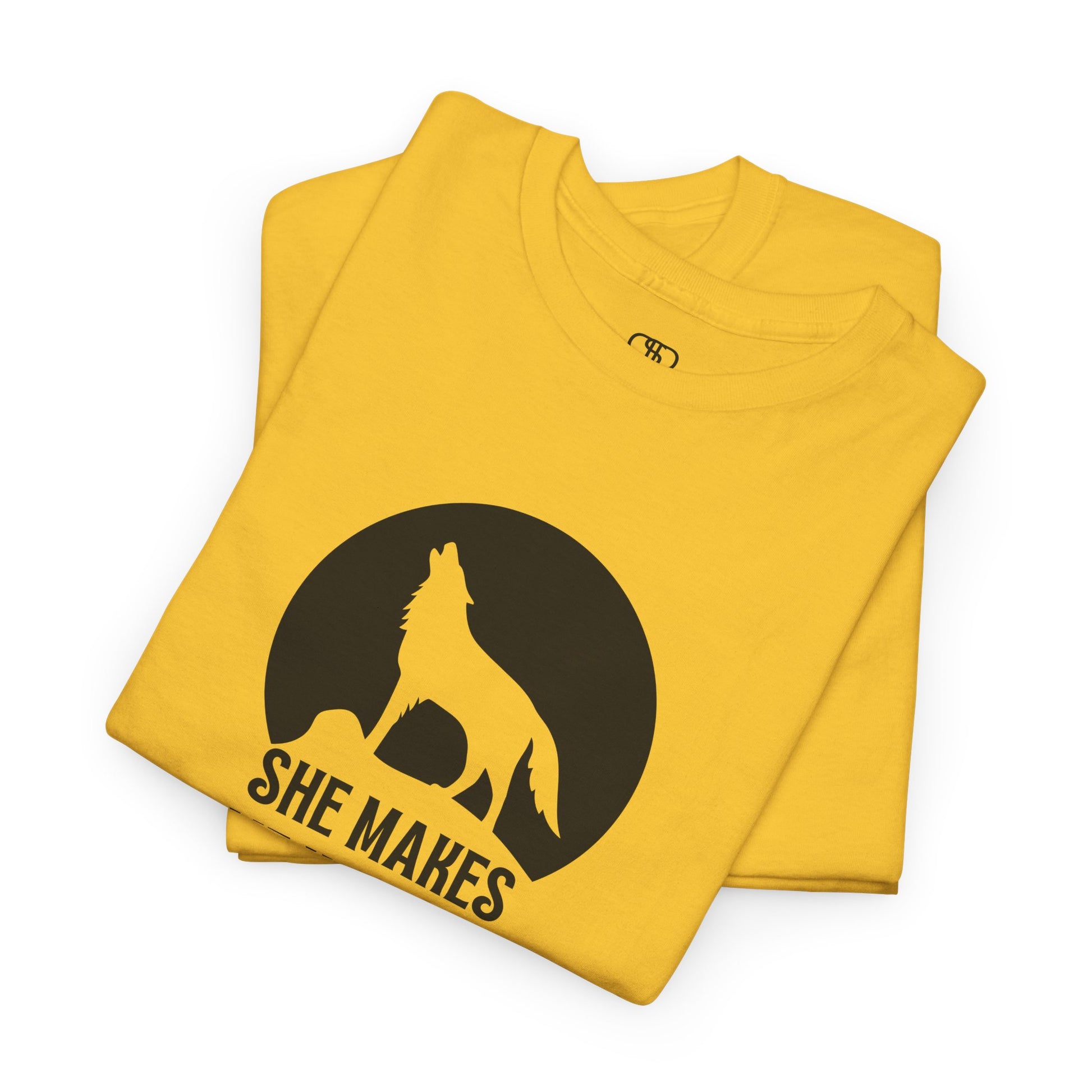 A folded daisy yellow T-shirt with a wolf silhouette howling at the moon on a cliff, and "She makes me HOOWWL" text.
