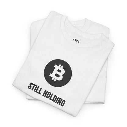 a FOLDED WHITE T-shirt with a Bitcoin emblem and "Still Holding" text in black.