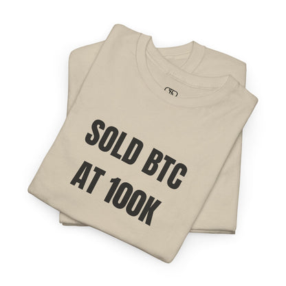 A folded ash gray T-shirt with bold text "SOLD BTC At 100K" on the front.