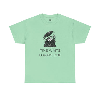 A close-up of a t-shirt with a gothic illustration. A black crow stands atop a weathered skull, which has moss and delicate vines growing through its eye sockets and around its form, blending nature and death.