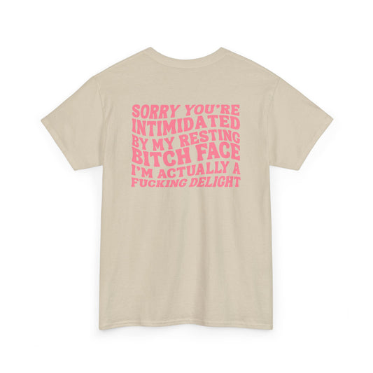 A sand t-shirt with a skeletal hand in a bubble on the front and the phrase “Sorry you’re intimidated by my resting Bitch ace I’m actually a fucking delight” on the back.