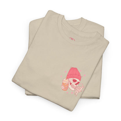 A SAND FOLDED T-shirt with a skeleton in a pink beanie holding a frozen coffee, snapping fingers, surrounded by sparkles graphic.